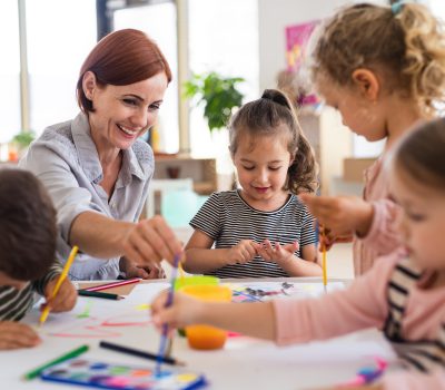 Group of small nursery school children with teacher indoors in classroom, painting